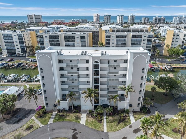 A multi-story hotel with a central courtyard, surrounded by palm trees and a marina with boats. - Casa Marina 432 Newly Remodeled, Water View 2 Bedroom Condo (Fort Myers Beach)