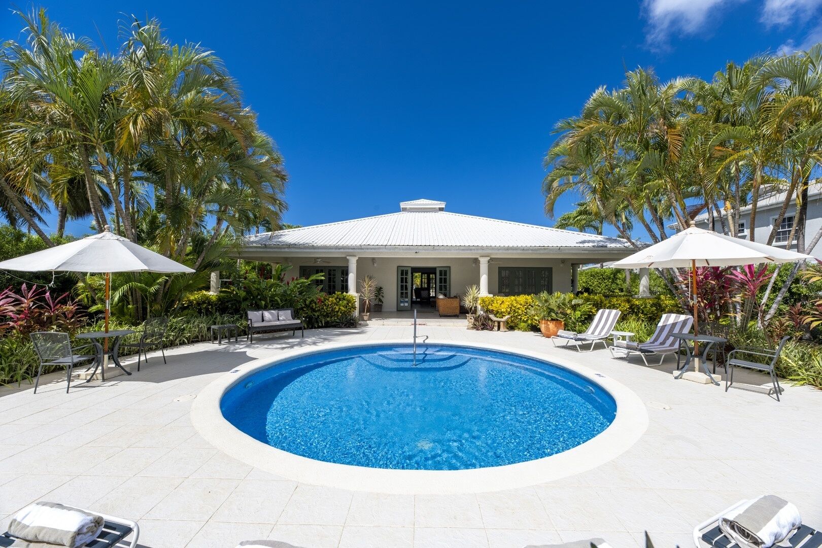 A pool area with a white-roofed building, palm trees, and lounge chairs.