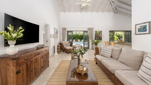 A spacious living room with a large flat-screen TV, a wooden cabinet, a wicker sofa, and a view of a pool through the open door. - Gibbs Glade Villa 3 Home (Gibbes)