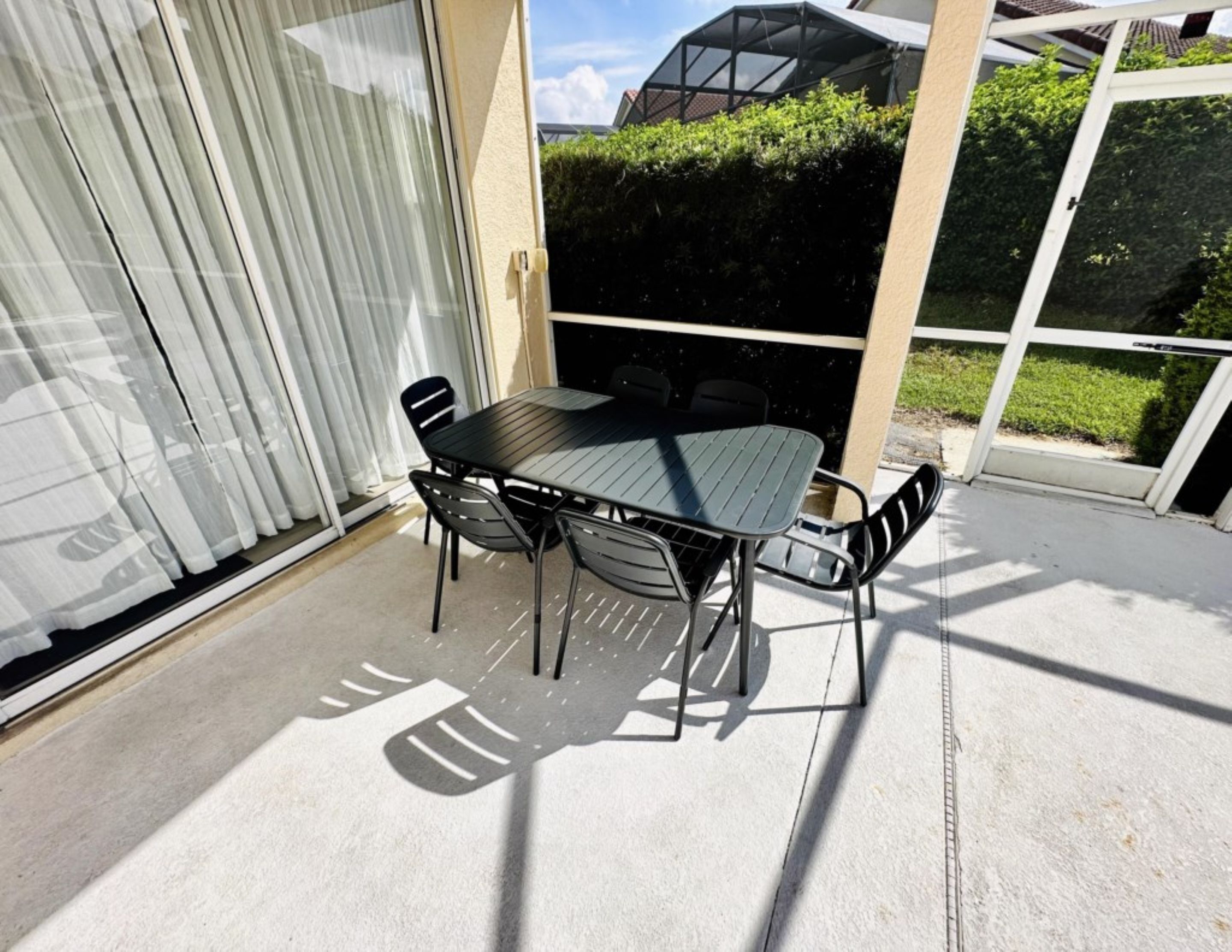 A patio with a table and chairs, a sliding glass door, and a view of a house and greenery.