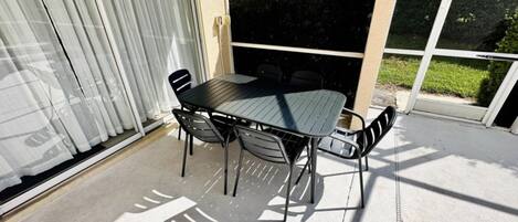 A patio with a table and chairs, a sliding glass door, and a view of a house and greenery.