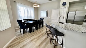 A modern kitchen with a stainless steel refrigerator, a granite countertop, and a dining area with a table and chairs. - Tranquilo Villa A Shine Villas Property In Tuscan Hills 5 Bedroom Villa (Davenport)
