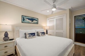 Ein Schlafzimmer mit Bett, Nachttischen, Deckenventilator, Fenster mit Jalousien und einem Wandbild.