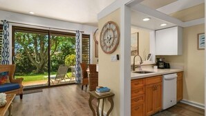 A modern kitchen with wooden cabinets, a built-in dishwasher, and a large window overlooking a garden.