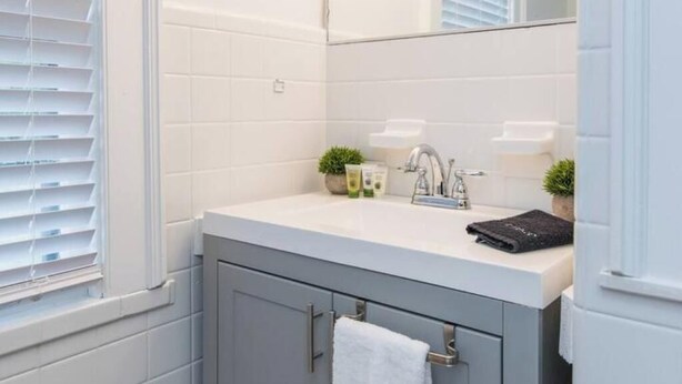 Un baño con lavamanos blanco, un espejo y un perchero para toallas.