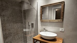 A modern bathroom with a glass-enclosed shower, a wooden vanity with a white sink, and a large mirror with an ornate frame. - La Maison Coloniale Suites (The Indies Rose) and Wellness Zone. (Cagliari)