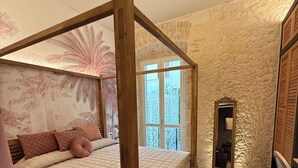 A bedroom with a four-poster bed, a large window, and a stone wall. - La Maison Coloniale Suites (The Indies Rose) and Wellness Zone. (Cagliari)