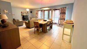 A spacious living area with a sofa, dining table, and chairs. There is a television and a lamp on a side table. - Apartment in Middelkerke Near the Beach (Middelkerke)