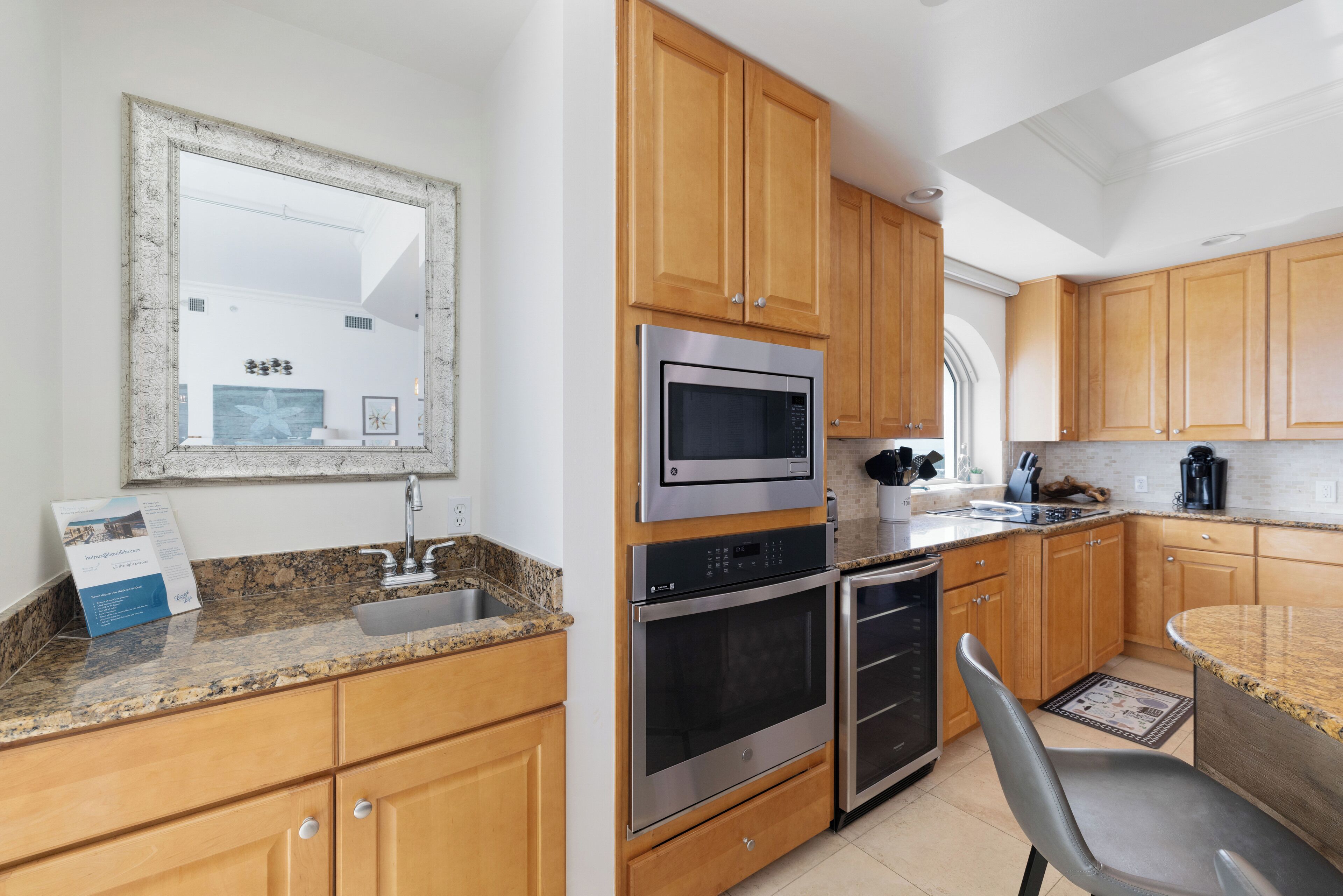 A modern kitchen with wooden cabinets, stainless steel appliances, granite countertops, and a large mirror.