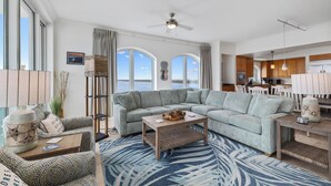 A spacious living area with a large sectional sofa, a coffee table, and a view of the outdoors through large windows.