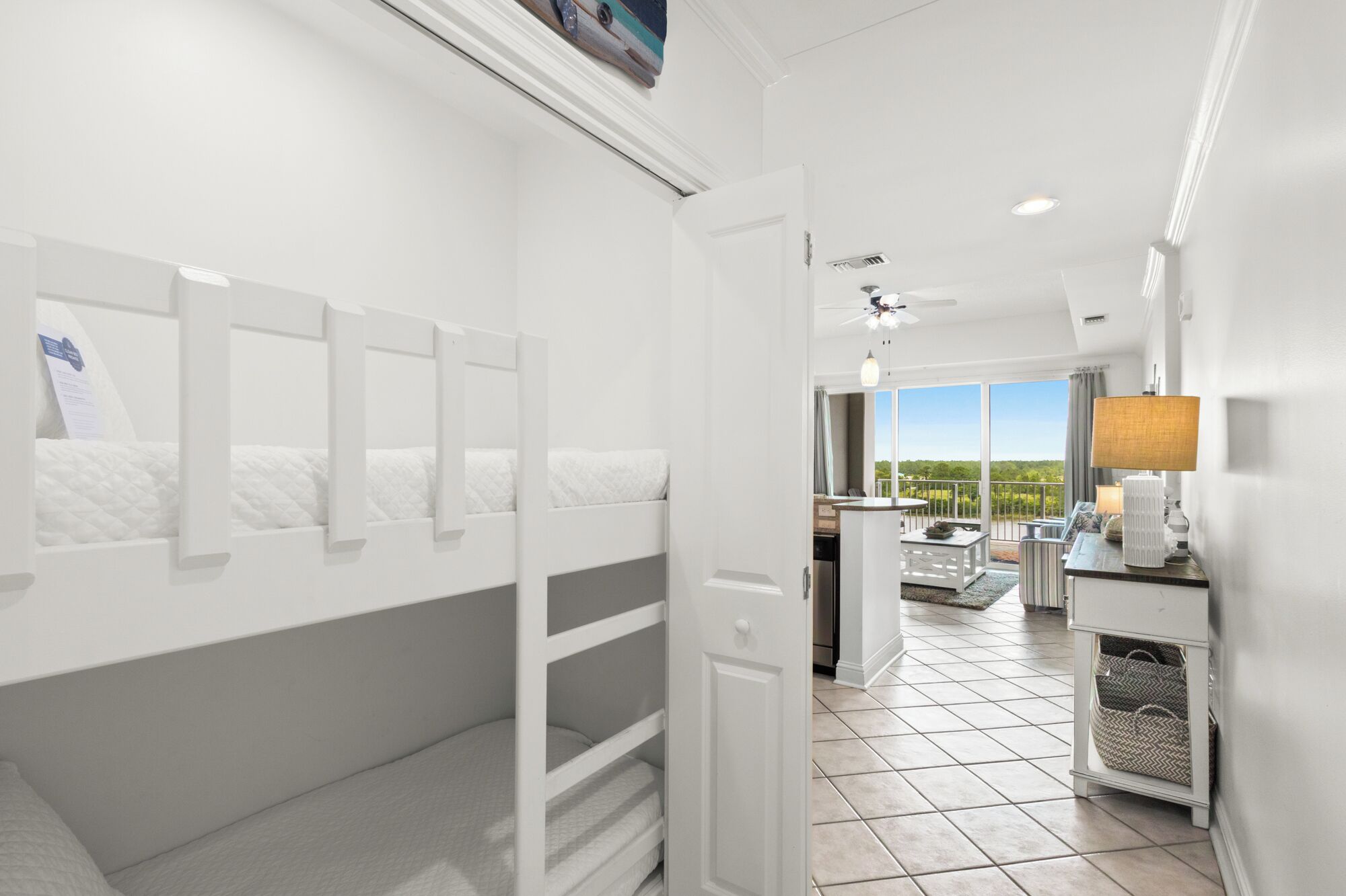 A hotel room with bunk beds, a balcony with a view, a kitchen area, and a large window.