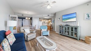 Un salon spacieux avec un canapé bleu, une table basse blanche et un téléviseur fixé au mur.