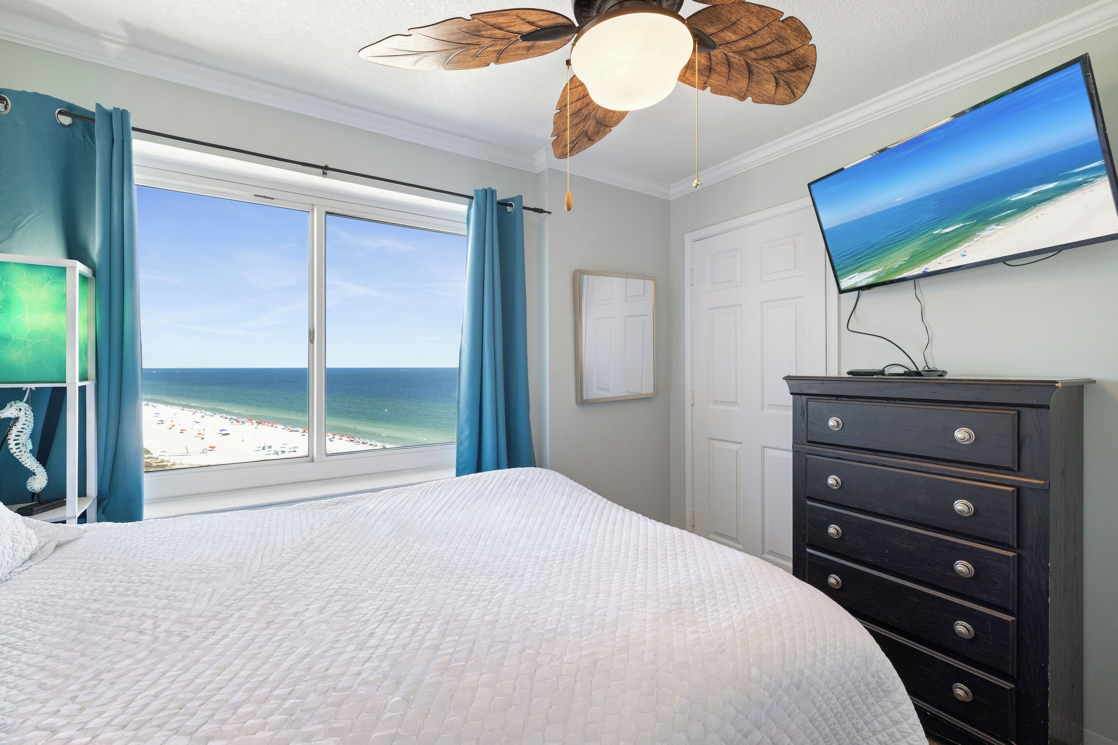 Una camera da letto con un letto grande, una cassettiera, una televisione e vista sulla spiaggia.
