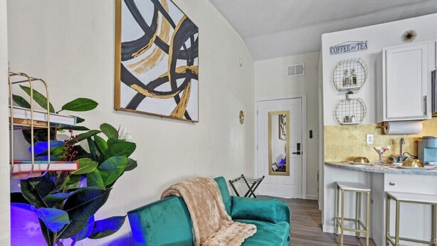 Un salon moderne avec un canapé de couleur turquoise, un coin cuisine décoré sur le thème du café et un grand tableau abstrait accroché au mur.