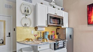 Une cuisine moderne avec des meubles blancs, un four à micro-ondes en acier inoxydable et un four encastré. On y trouve deux tabourets de couleur dorée au comptoir et un petit îlot central doté d’un plan de travail en marbre.