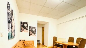 Un espace de vie compact comprenant un canapé, une petite table, une table à manger avec des chaises et des œuvres d’art accrochées aux murs.
