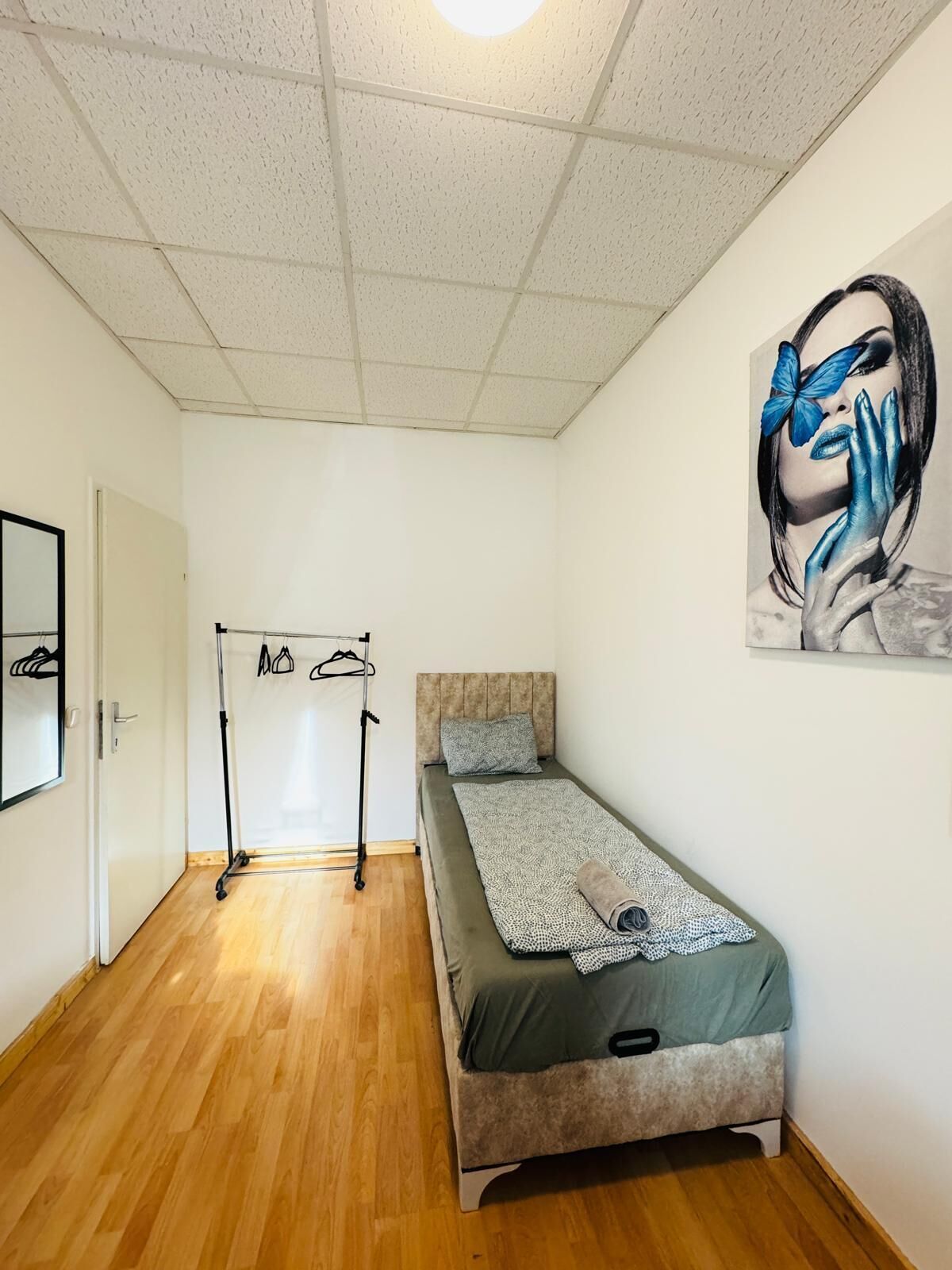 A small, neatly arranged bedroom with a single bed, a wardrobe, and a coat rack.
