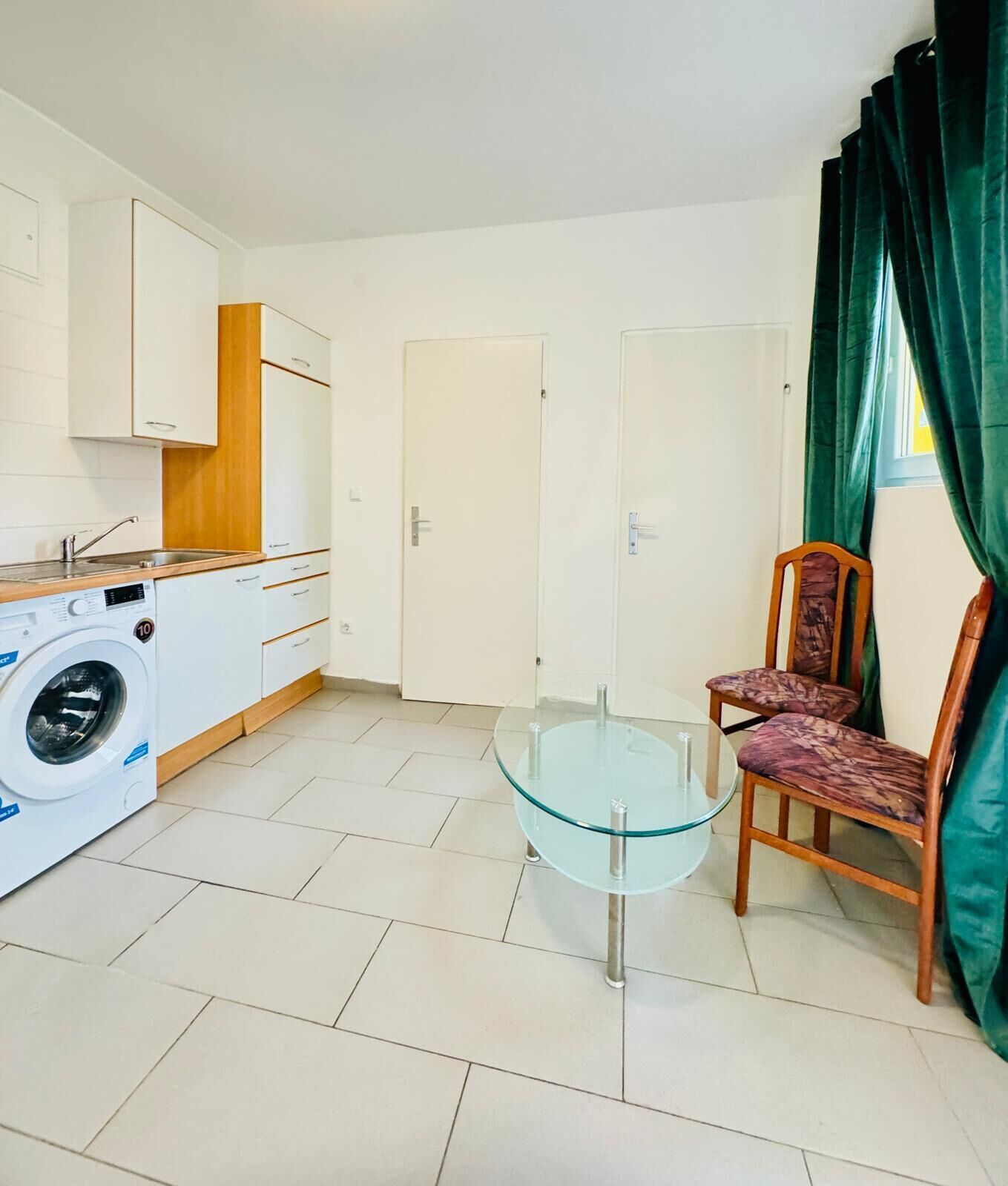 Un espacio habitable compacto con lavadora, una mesa de vidrio, dos sillas y una puerta.