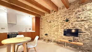 A modern kitchen with a stone wall, wooden beams, and a flat-screen TV mounted on the wall. - Agi Porthos 800 Apartamento for rent in Roses Girona. (Roses)