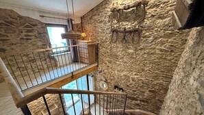 A multi-level stone interior with a wooden staircase, a hanging lamp, and a rustic wall decor. - Agi Porthos 800 Apartamento for rent in Roses Girona. (Roses)