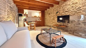 A cozy living room with a sofa, a coffee table, and a TV. There's a kitchen in the background with a stone wall. - Agi Porthos 800 Apartamento for rent in Roses Girona. (Roses)