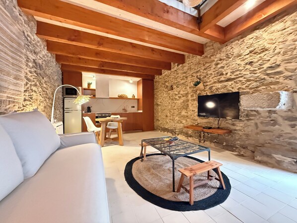 A cozy living room with a sofa, a coffee table, and a TV. There's a kitchen in the background with a stone wall. - Agi Porthos 800 Apartamento for rent in Roses Girona. (Roses)