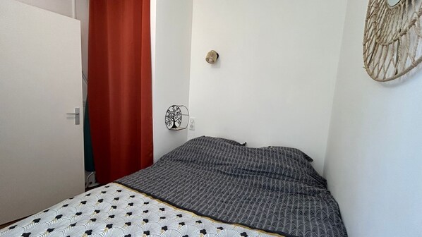 Un dormitorio con cama, cortina roja, luz de pared y un adorno en la pared.