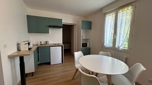 Une cuisine compacte équipée d’un lave-vaisselle, d’un four à micro-ondes et d’un petit réfrigérateur. On y trouve une table à manger avec quatre chaises et une fenêtre avec des rideaux.