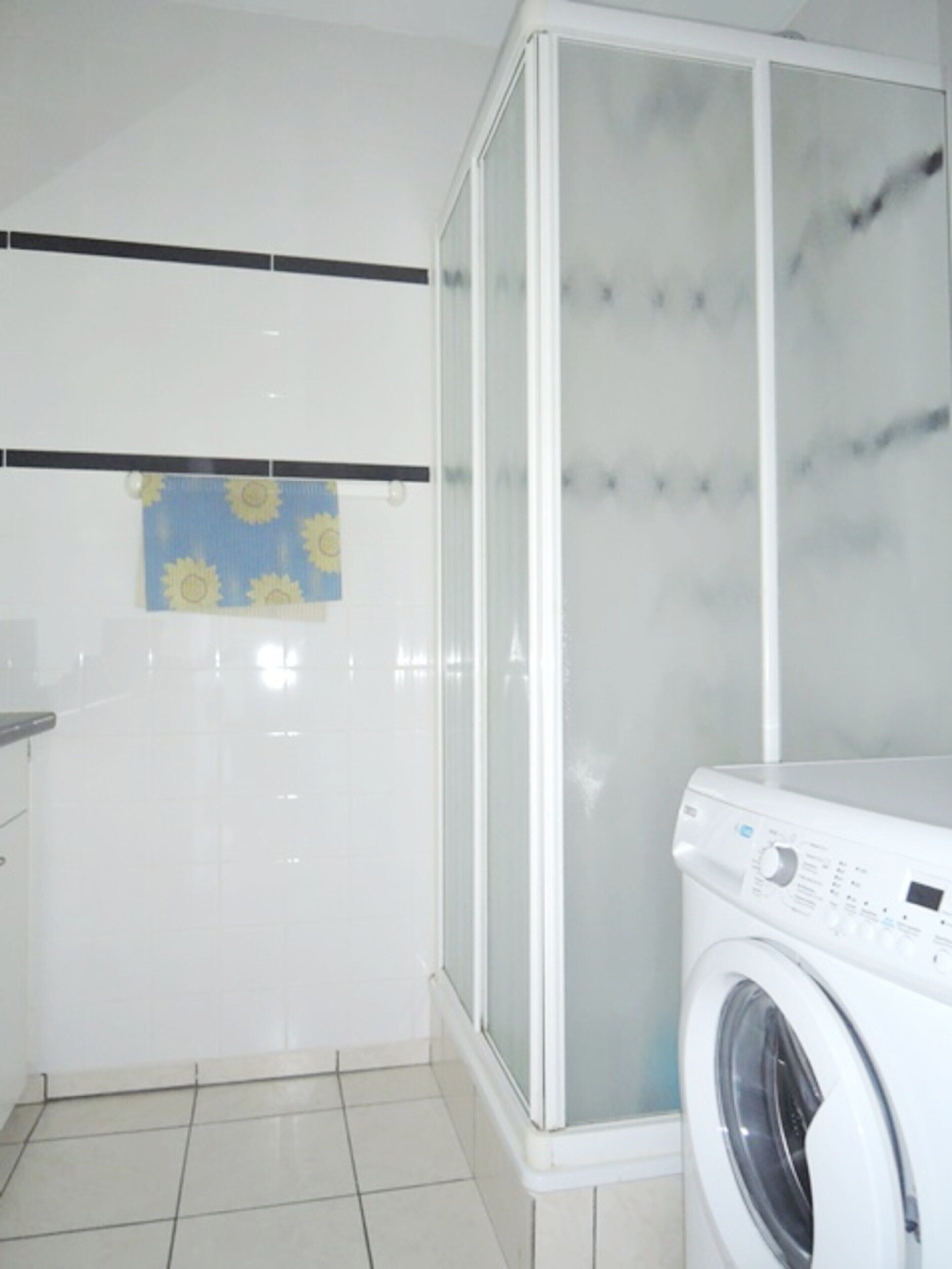 A laundry room with a washing machine, a glass-enclosed dryer, and a tiled floor.
