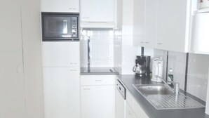 Une cuisine moderne avec des meubles blancs, un four à micro-ondes, une machine à café et un évier.