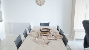 Une salle à manger moderne avec une table rectangulaire, huit chaises, une horloge au mur et un radiateur en dessous.