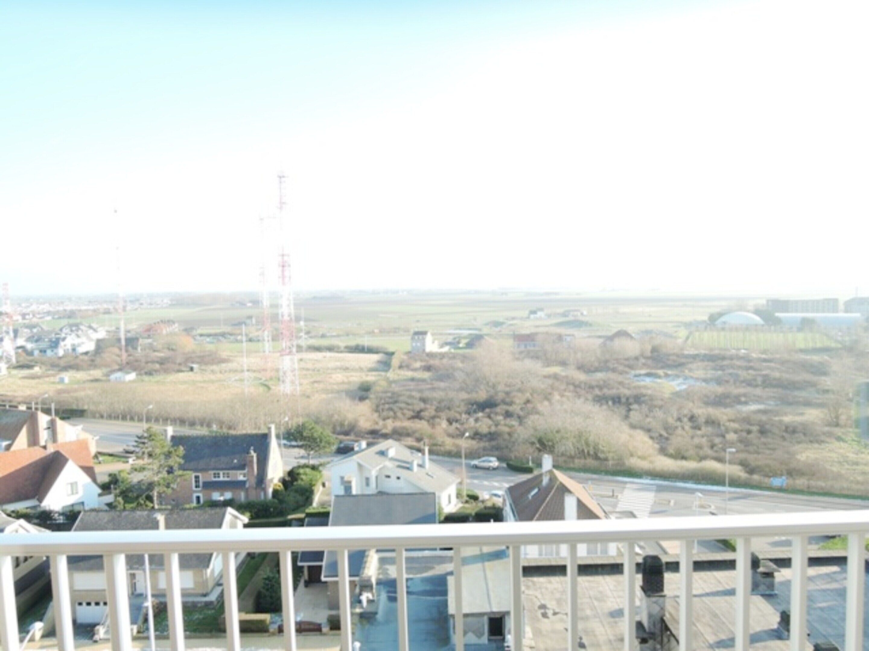 Zona residencial con casas, una calle y una torre de transmisión eléctrica a lo lejos.