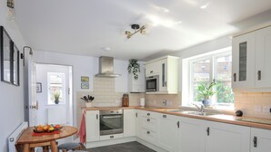 Una cucina moderna con mobili bianchi, un piano di lavoro in legno e un forno integrato. C'è una zona pranzo con tavolo e sedie, e una finestra che lascia entrare luce naturale.