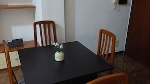 Een kleine, donkere tafel met een bloevas, twee houten stoelen en een laptop op een houten kast.