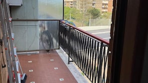 Een balkon met een metalen hekwerk, uitzicht op een straat en een gebouw op de achtergrond.