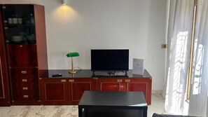 Una habitación de hotel con un armario de madera, un televisor sobre un soporte, un escritorio y una lámpara.