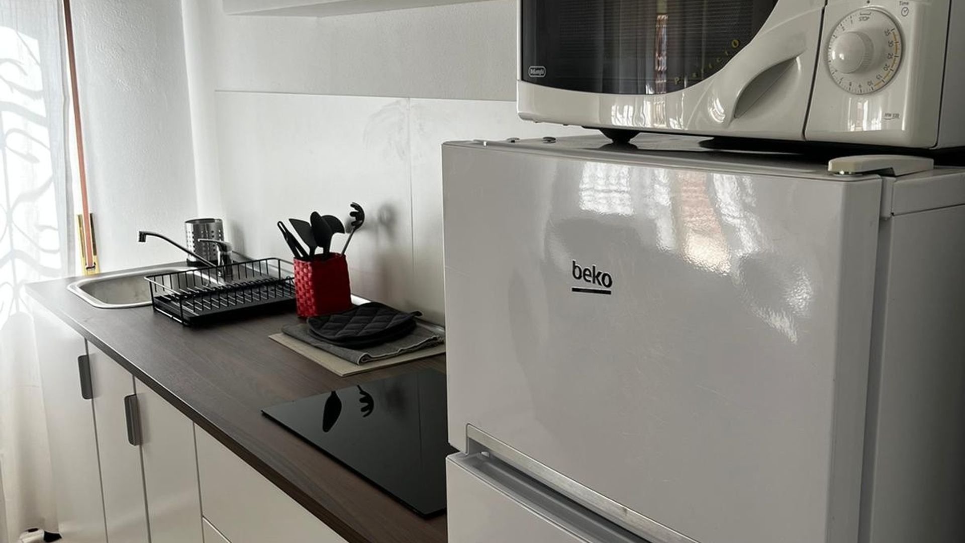 Una kitchenette con microondas, hervidor y un portalapilas rojo en la encimera.