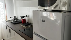 Una kitchenette con microondas, hervidor y un portalapilas rojo en la encimera.