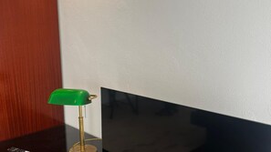 Una habitación con piso de madera, una mesa negra y una lámpara de escritorio verde.