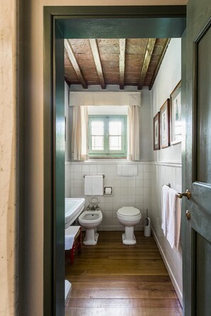 Une petite salle de bain avec un plancher en bois, deux toilettes, un lavabo et une fenêtre avec des rideaux.