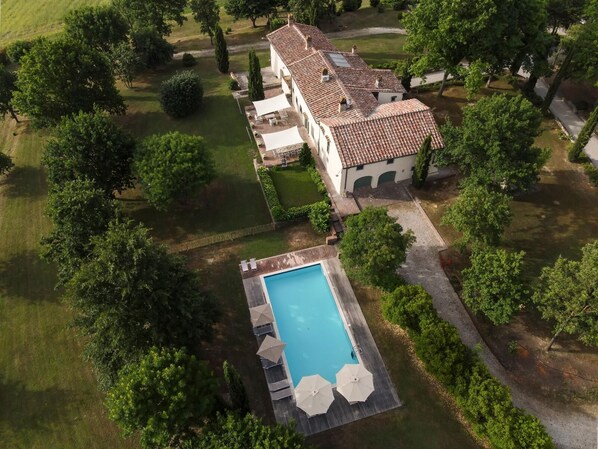 Une grande maison avec une piscine, entourée d’une végétation luxuriante et d’arbres.