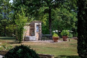 Une construction rustique en pierre, dotée d’une petite fenêtre et entourée d’une végétation luxuriante et de plantes en pot.