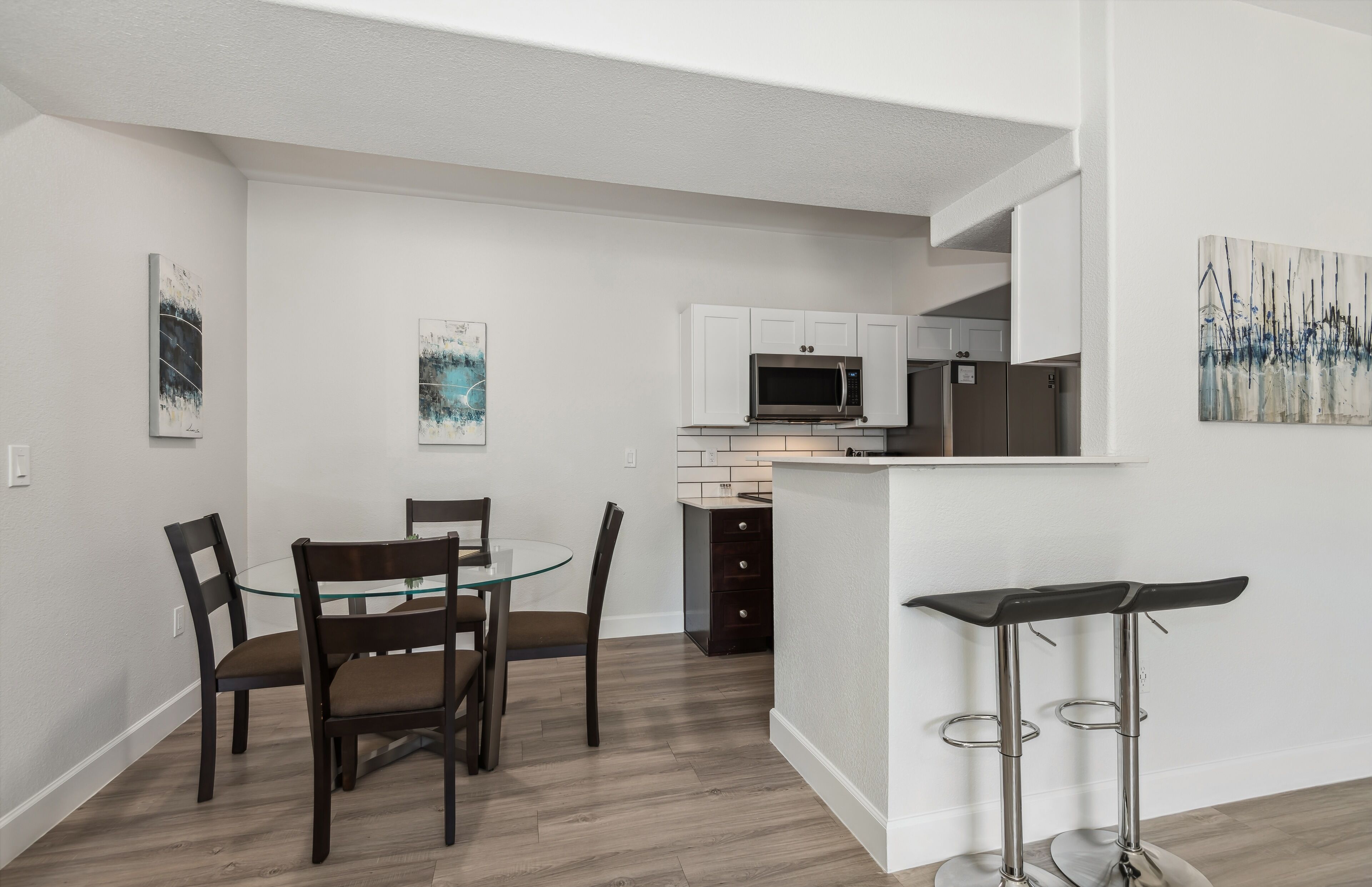 A modern kitchen with white cabinets, a stainless steel microwave, and a small island with a bar stool.
