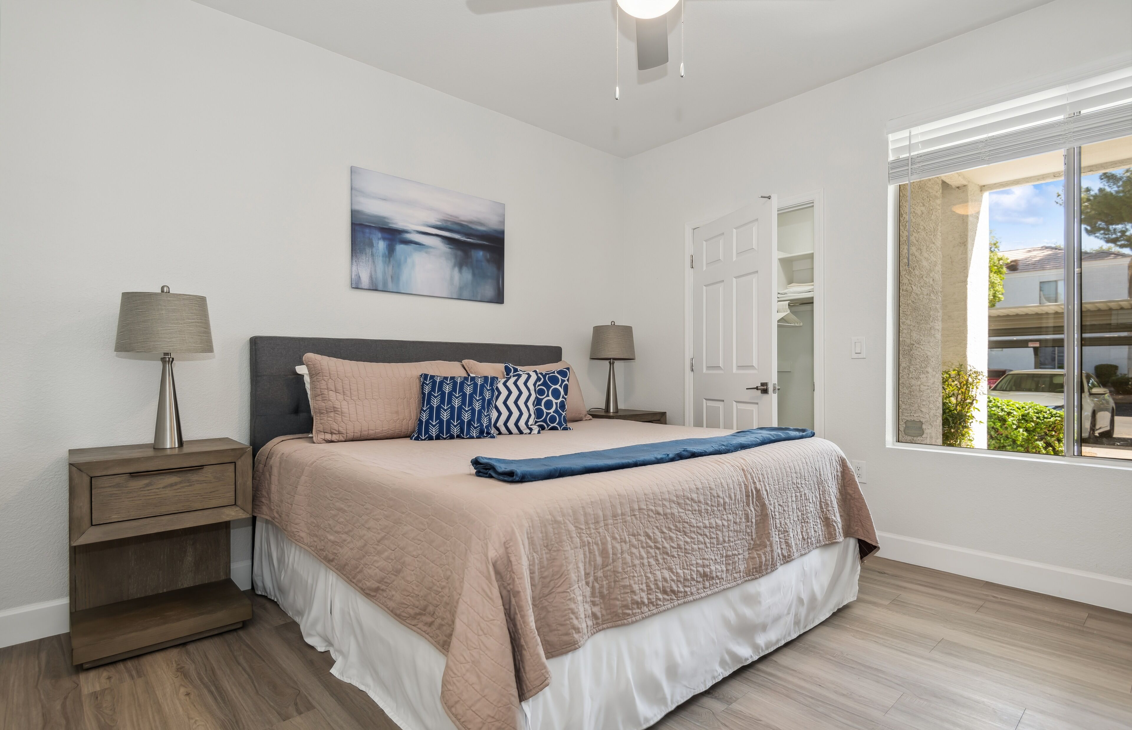 Une chambre à coucher moderne avec un lit, deux tables de chevet, une fenêtre donnant sur un beau paysage et un tableau accroché au mur.