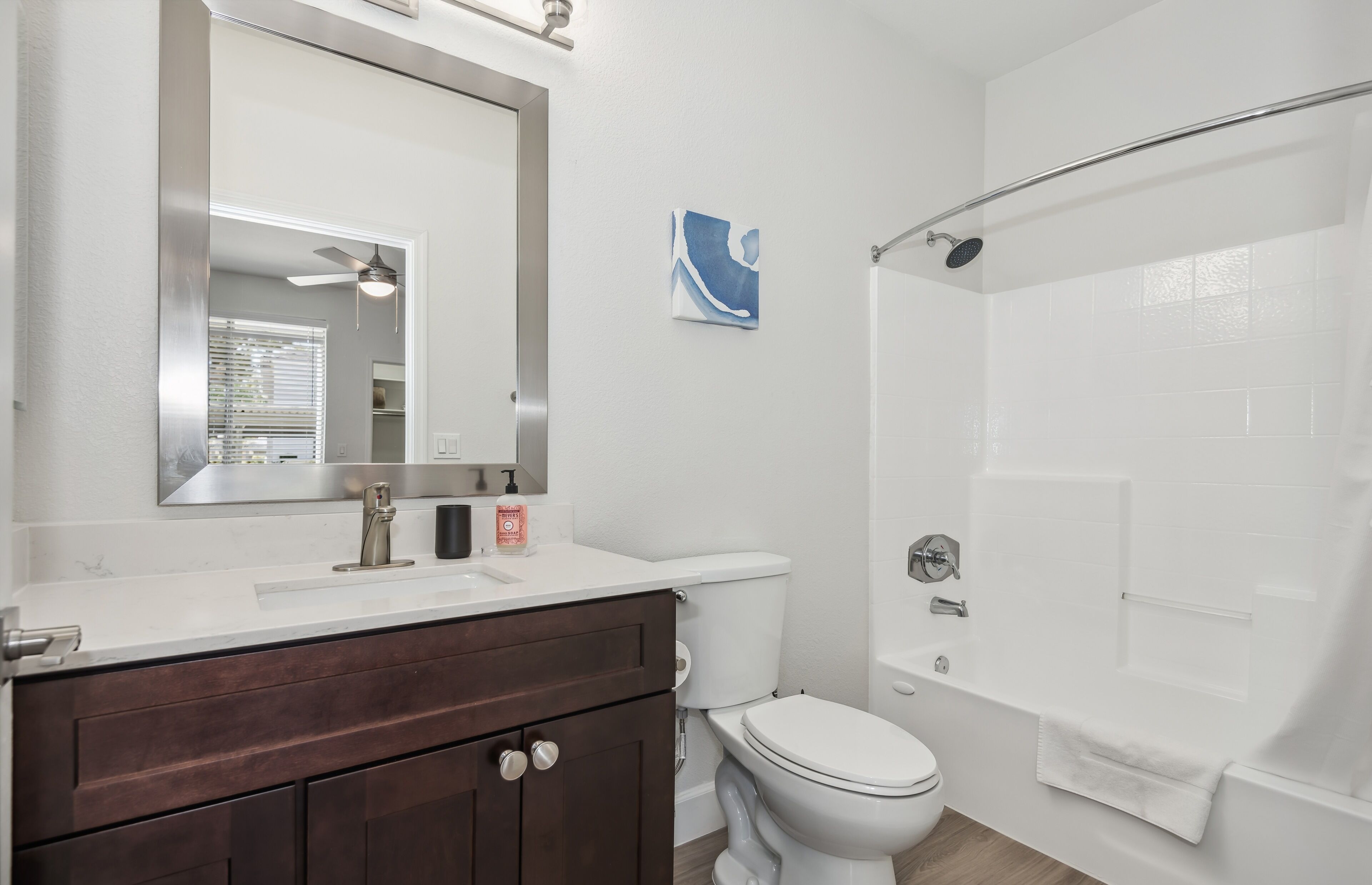 A bathroom with a white toilet, a shower, a vanity with a mirror, and a towel rack.
