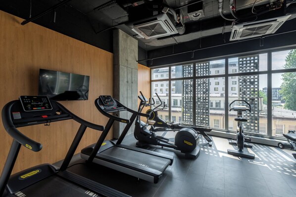 Une salle de sport équipée de tapis de course, de vélos elliptiques et d’appareils de musculation, avec de grandes fenêtres et un téléviseur fixé au mur.