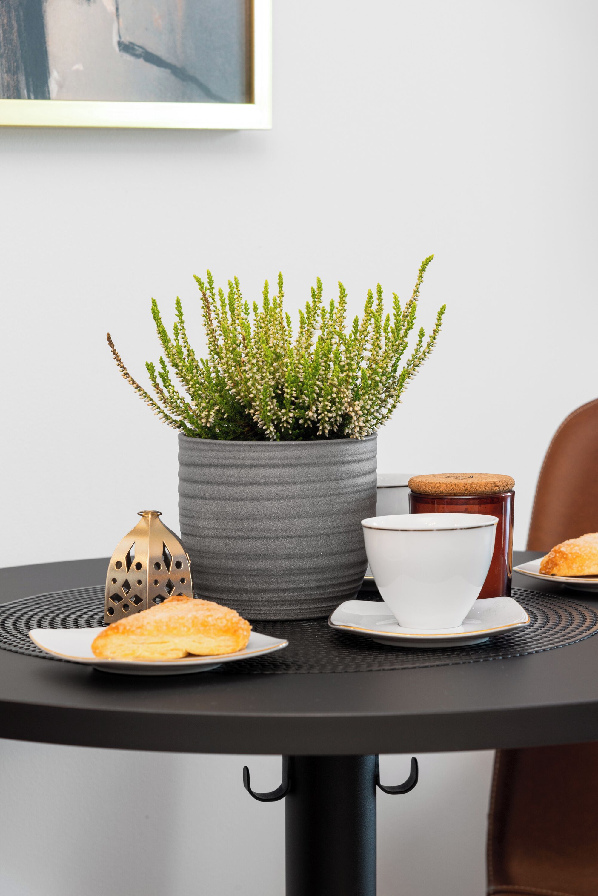 Una mesa de comedor con una planta en maceta, un farol decorativo, un cuenco blanco y un plato con comida.