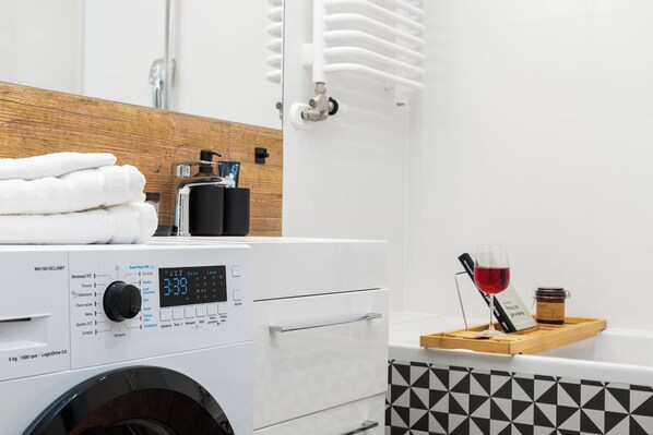 Une salle de bain moderne équipée d’un lave-linge, d’un plan de travail en bois avec des serviettes, d’un verre à vin et d’un plateau avec une bouteille.