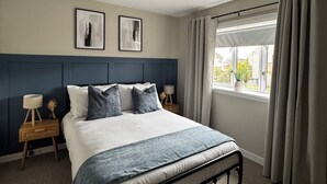 A bedroom with a bed, two bedside tables, a window with curtains, and two framed pictures on the wall.