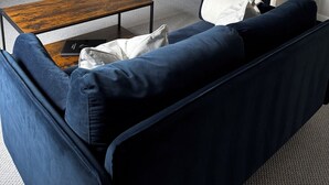 A modern living room with a dark blue sofa, a wooden coffee table, and a flat-screen TV mounted on the wall.